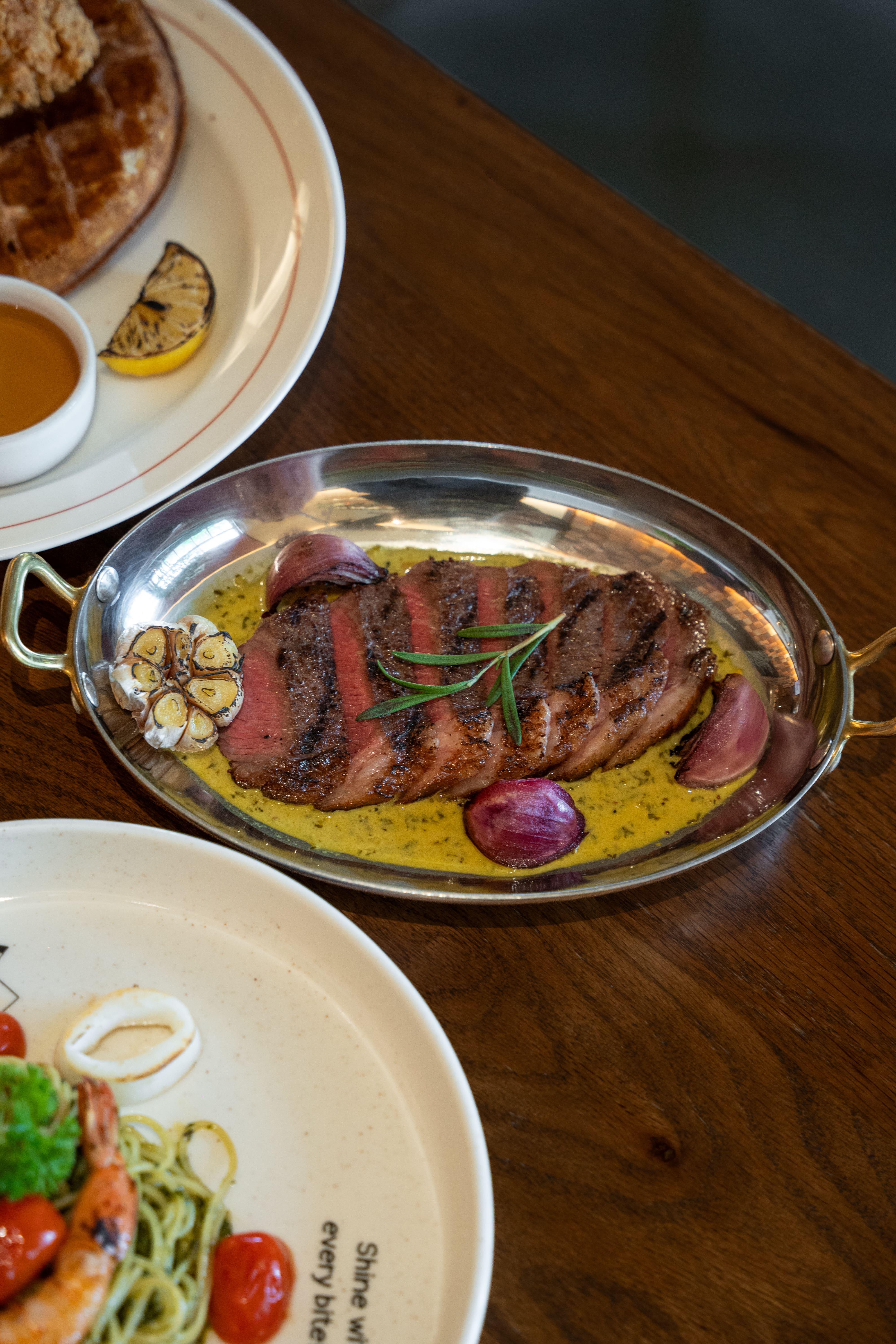 Juicy sliced grilled steak served with roasted garlic, red onions, rosemary and a rich sauce at CouCou All Day Bangkok.