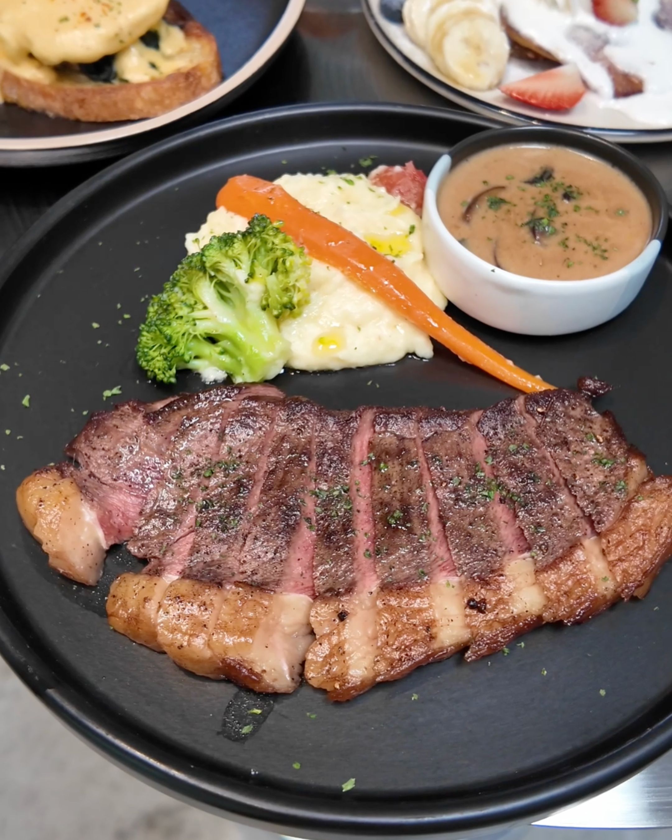 A juicy grilled steak sliced into tender pieces, served with mashed potatoes, broccoli, carrots and sauce at JUNE. Cafe Bangkok.