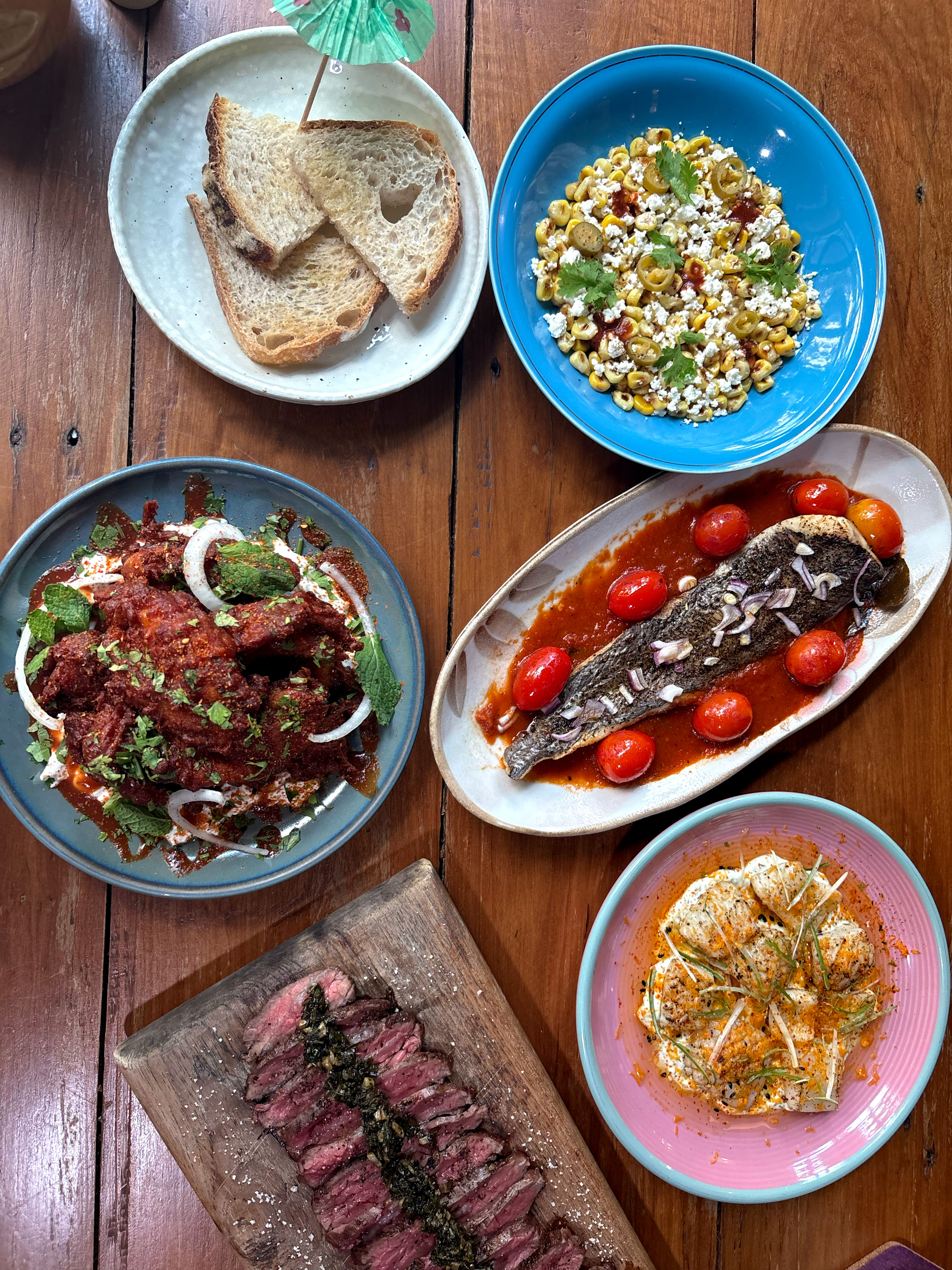 A shared spread of grilled fish, flank steak, fried chicken and corn salad at Mad Moa, Bangkok