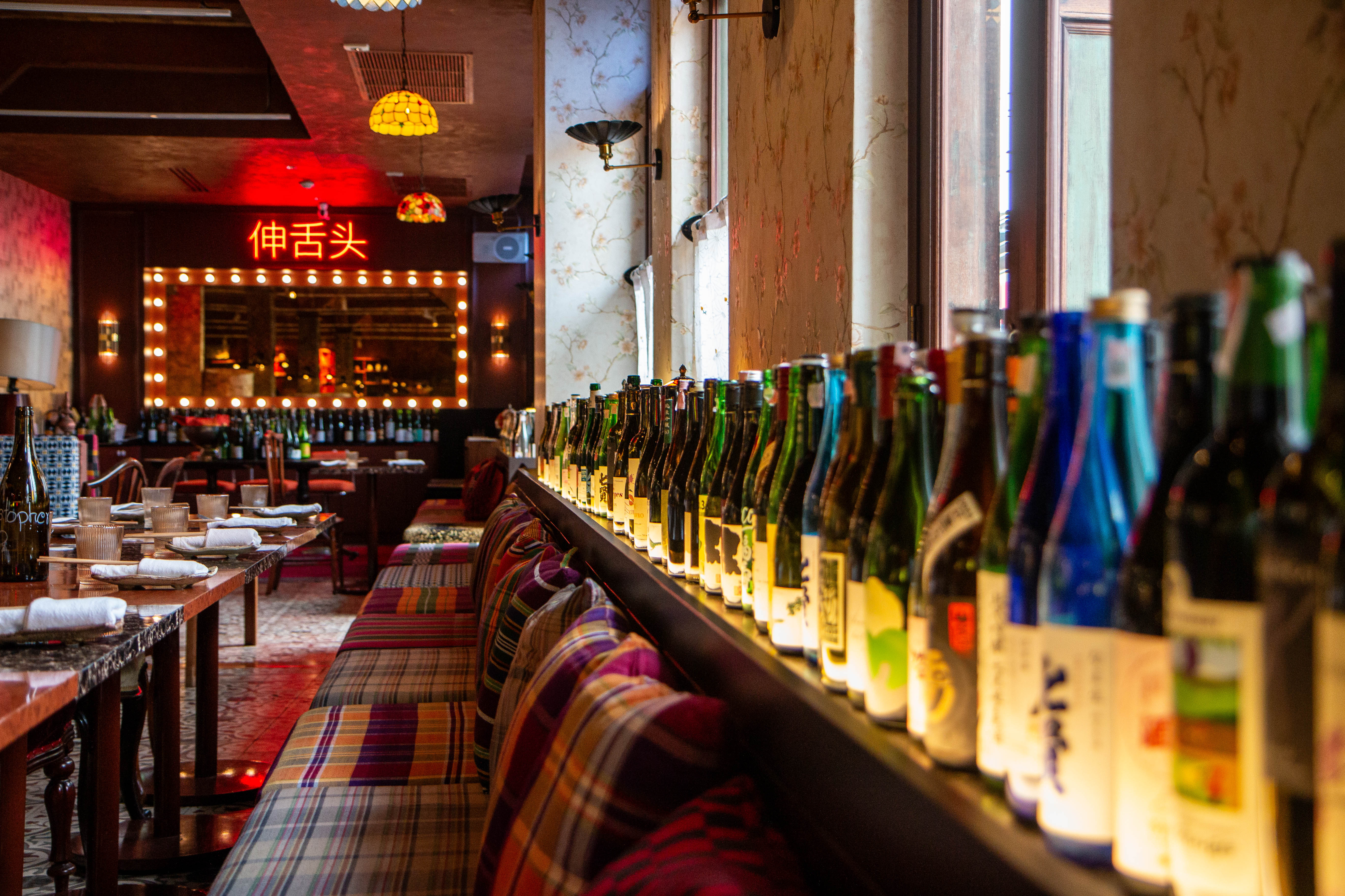 Cozy interior of Namsu Shan Izakaya in Bangkok featuring a long bar lined with sake bottles and vintage Tiffany-style lamps.