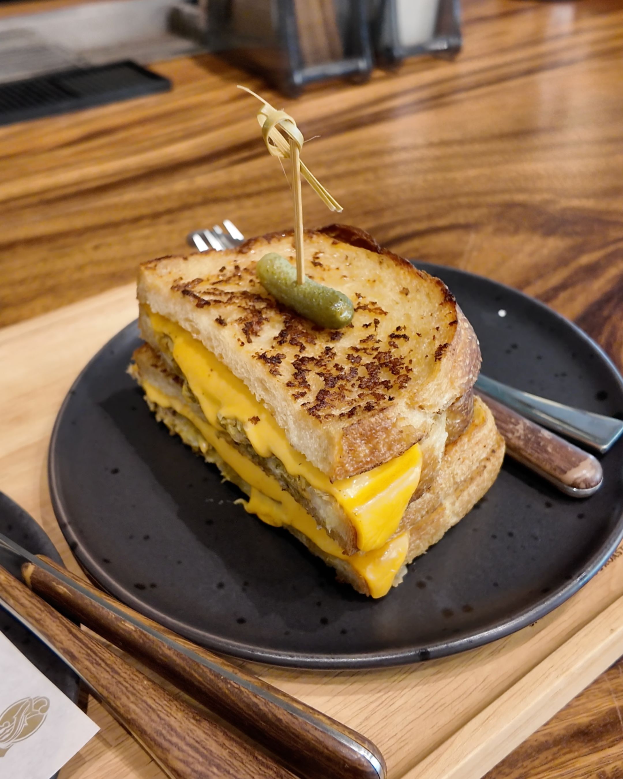Enjoy a toasted sandwich filled with melted cheese and a savory filling, served on a black plate at The Old School Specialty Coffee Bangkok.