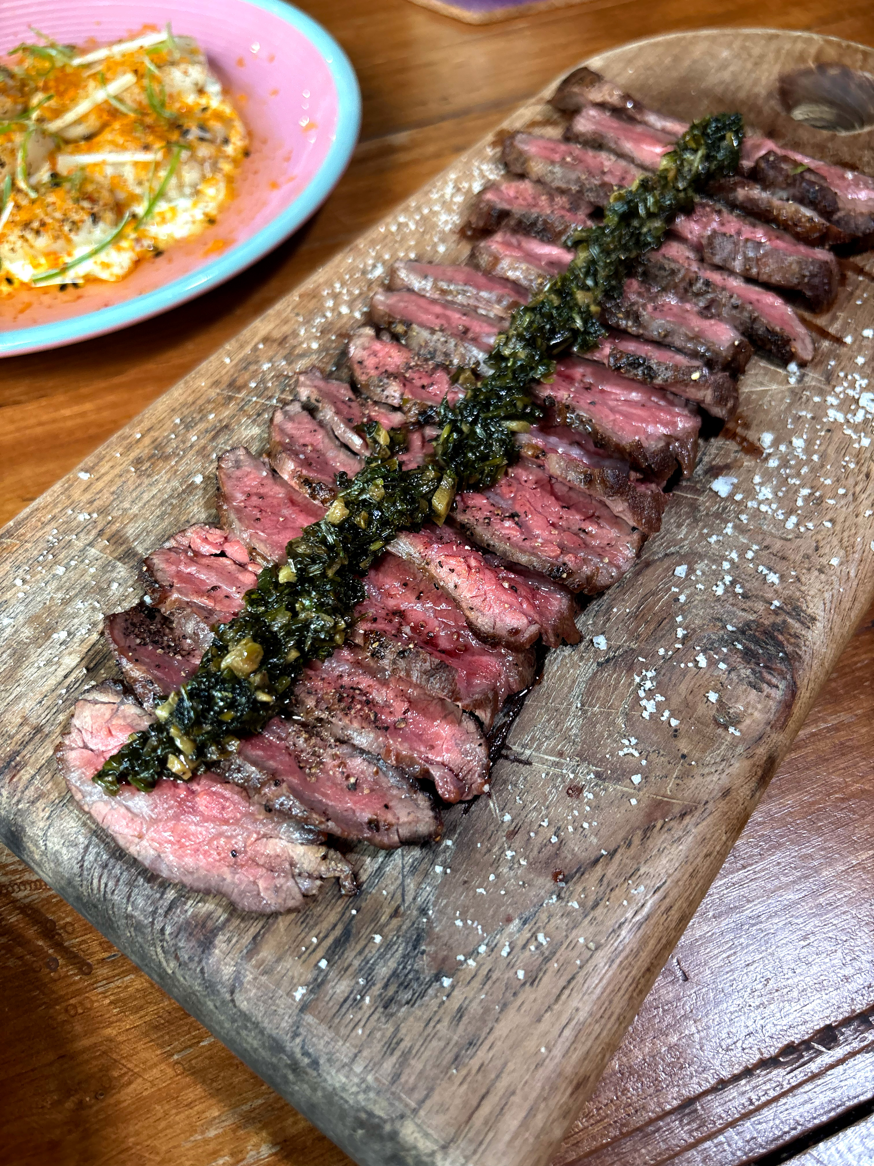 Sliced flank steak with chimichurri and sea salt on a wooden board at Mad Moa restaurant in Bangkok