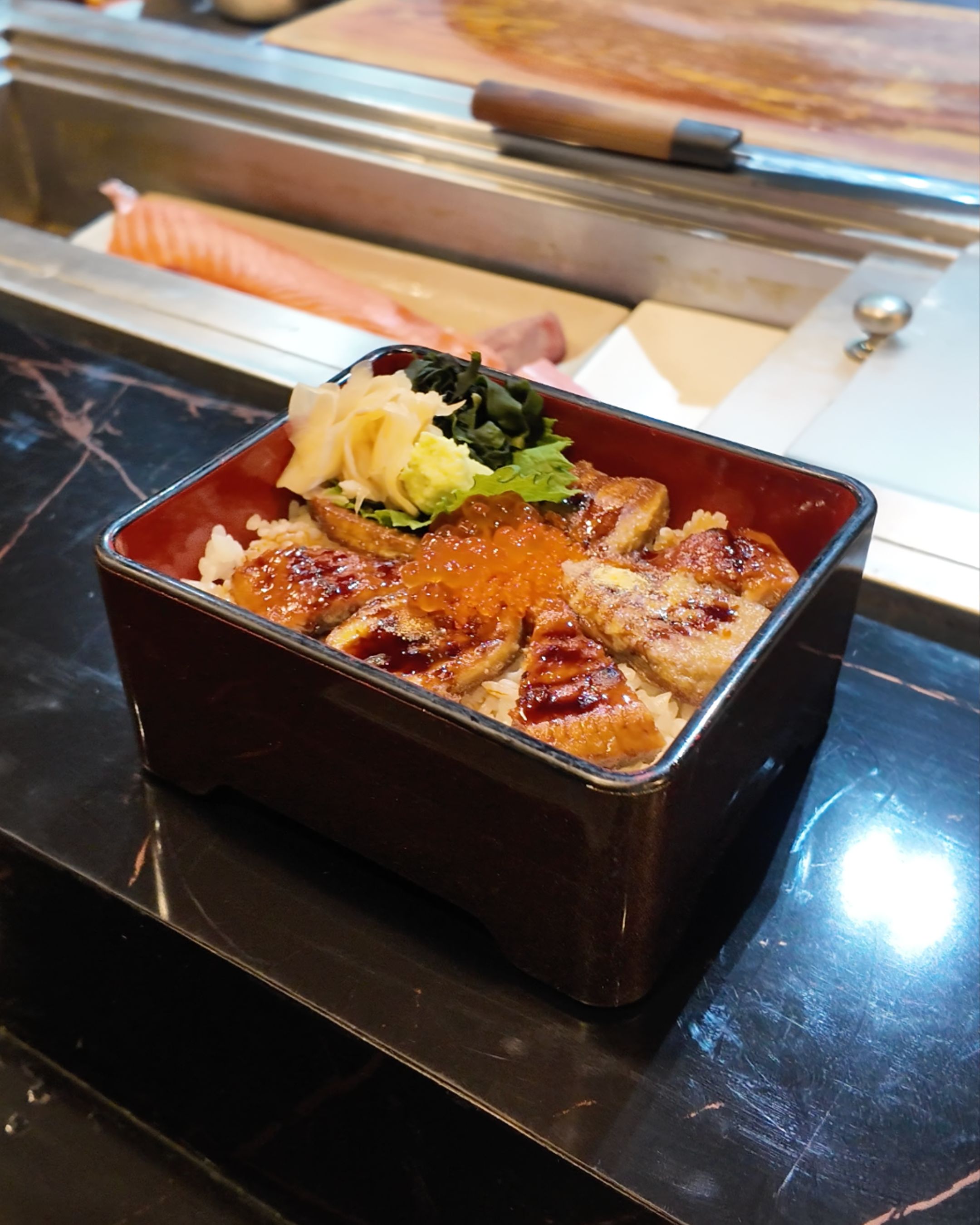 A traditional Japanese rice dish topped with grilled eel, savory sauce and fresh garnishes, showcasing the variety of Japanese cuisine at YAWA Bangkok.