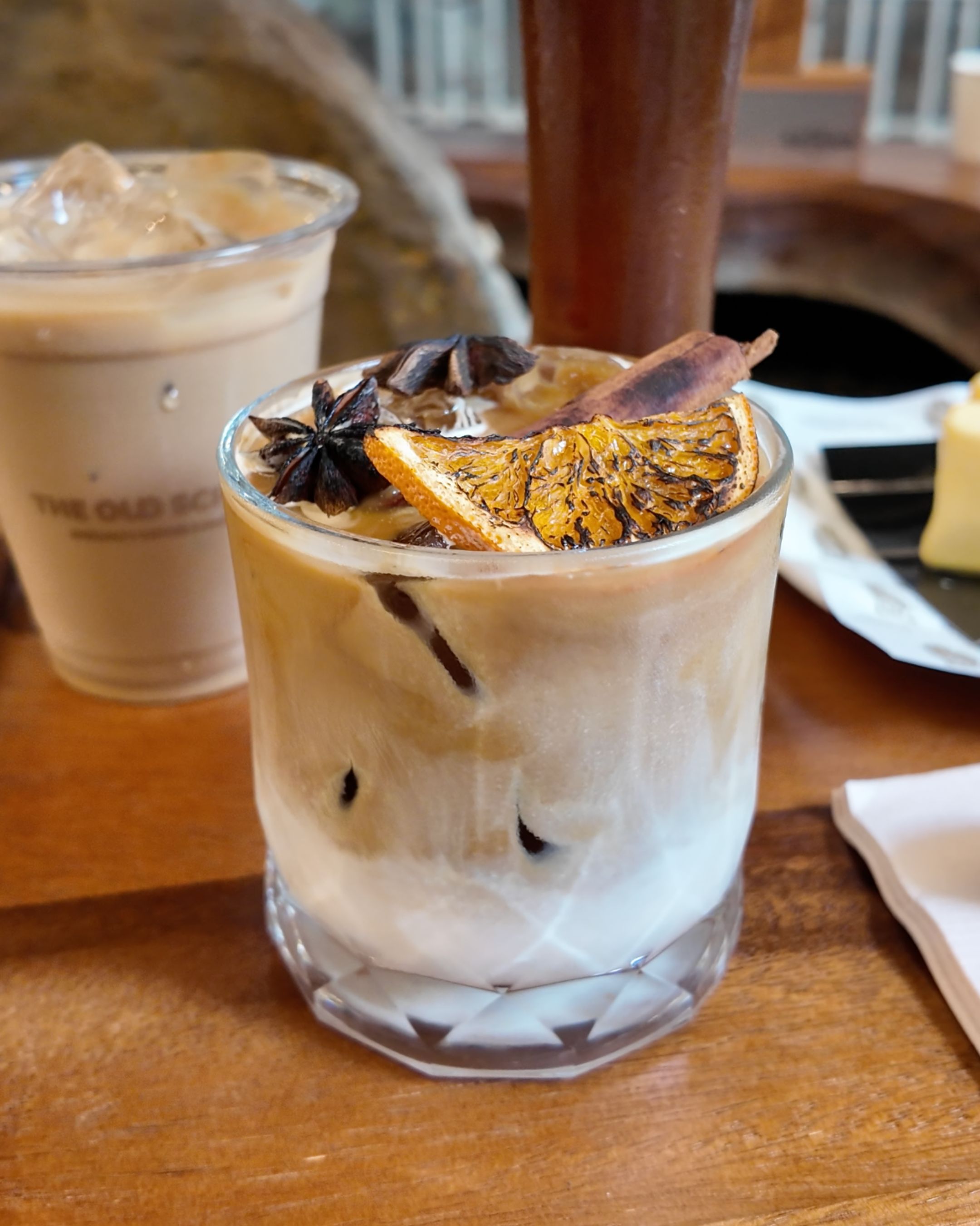 Discover a creamy iced coffee topped with dried citrus and aromatic garnishes, beautifully presented at The Old School Specialty Coffee in Bangkok.