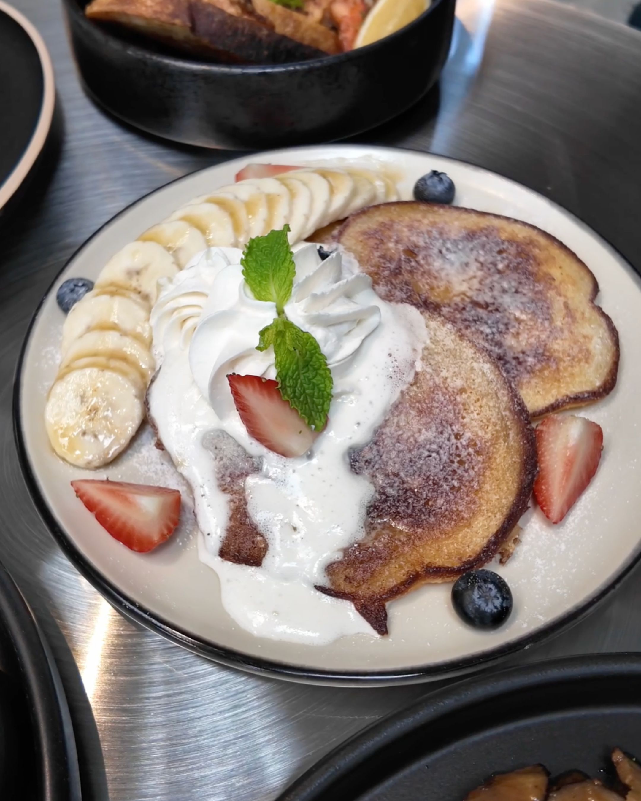 Golden French toast topped with whipped cream, fresh strawberries, banana slices and mint leaves, offering a delicious sweet brunch option at JUNE. Cafe Bangkok.