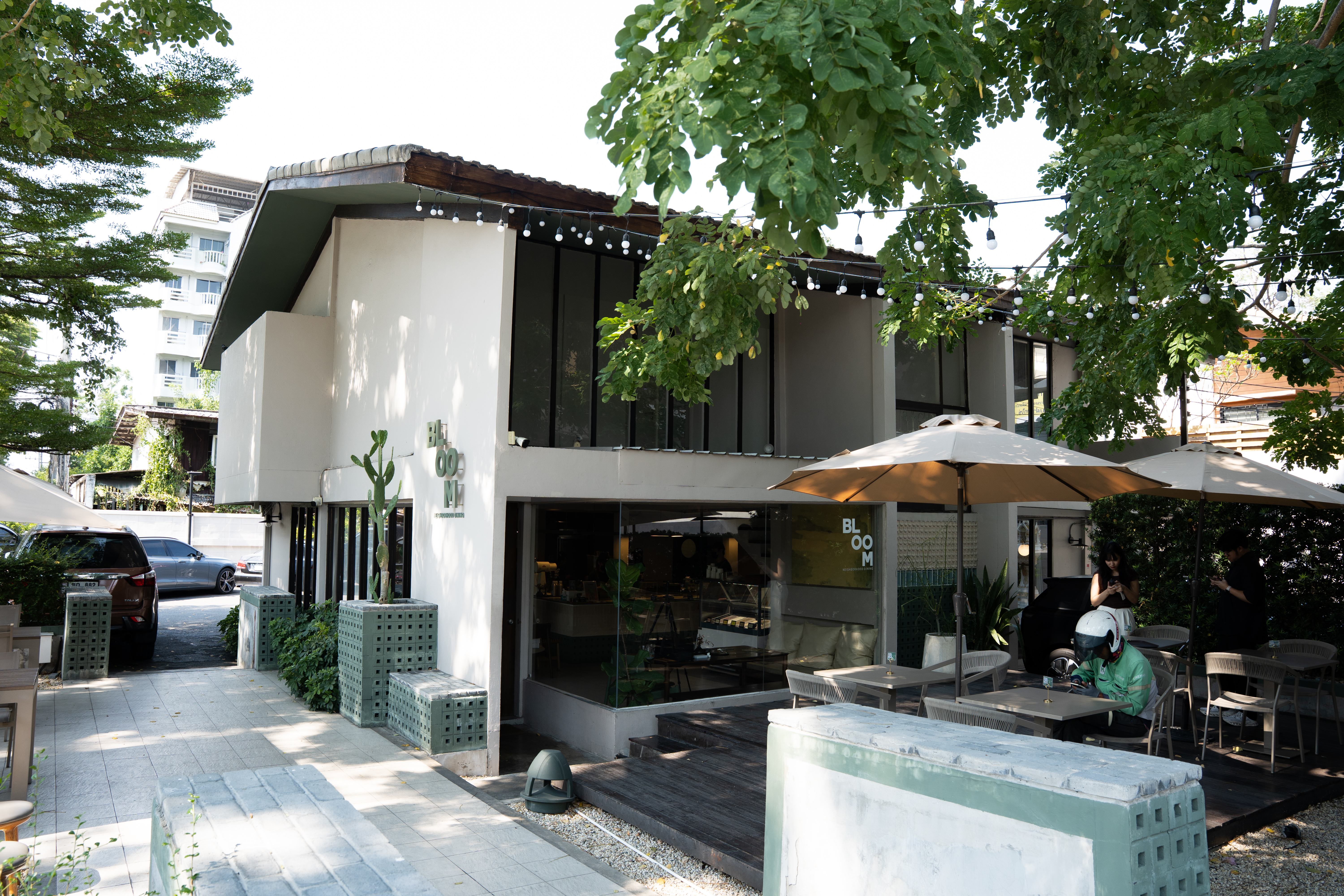Bloom Dining Rama 9 outdoor seating area with minimalist tables and chairs under sun umbrellas in a shaded garden setting